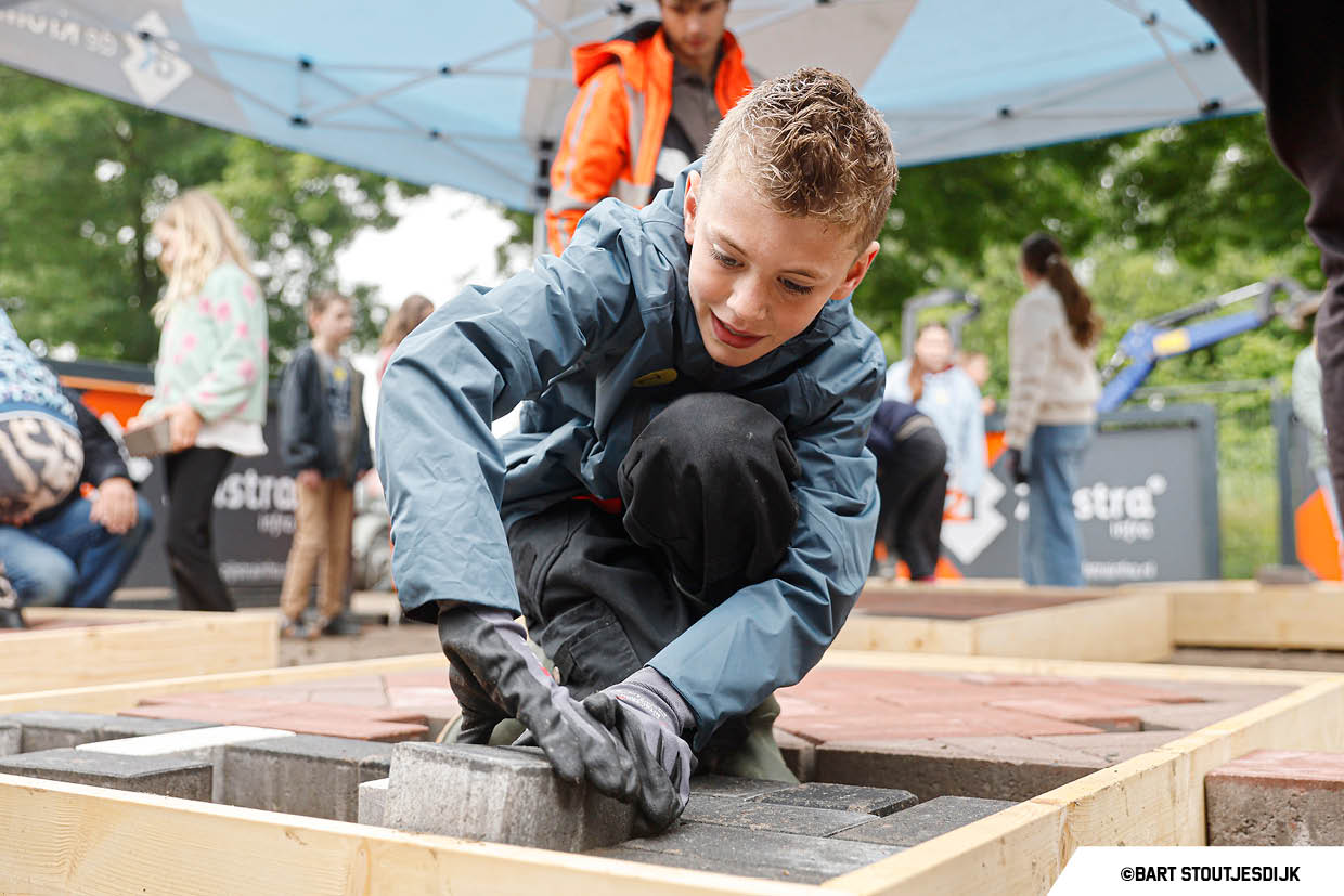 Jongen legt met handschoenen aan straatstenen bij de Onderwijsdag van de bouw