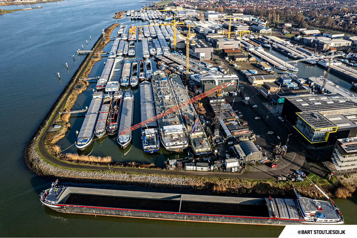 Luchtfoto van een scheepswerf met liggende binnenschepen langs de rivier