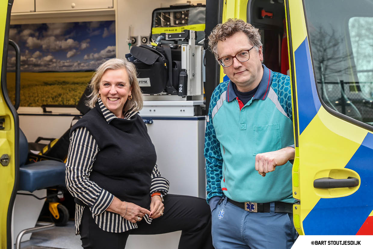 Verpleegkundige en collega poseren bij de open deur van een ambulance