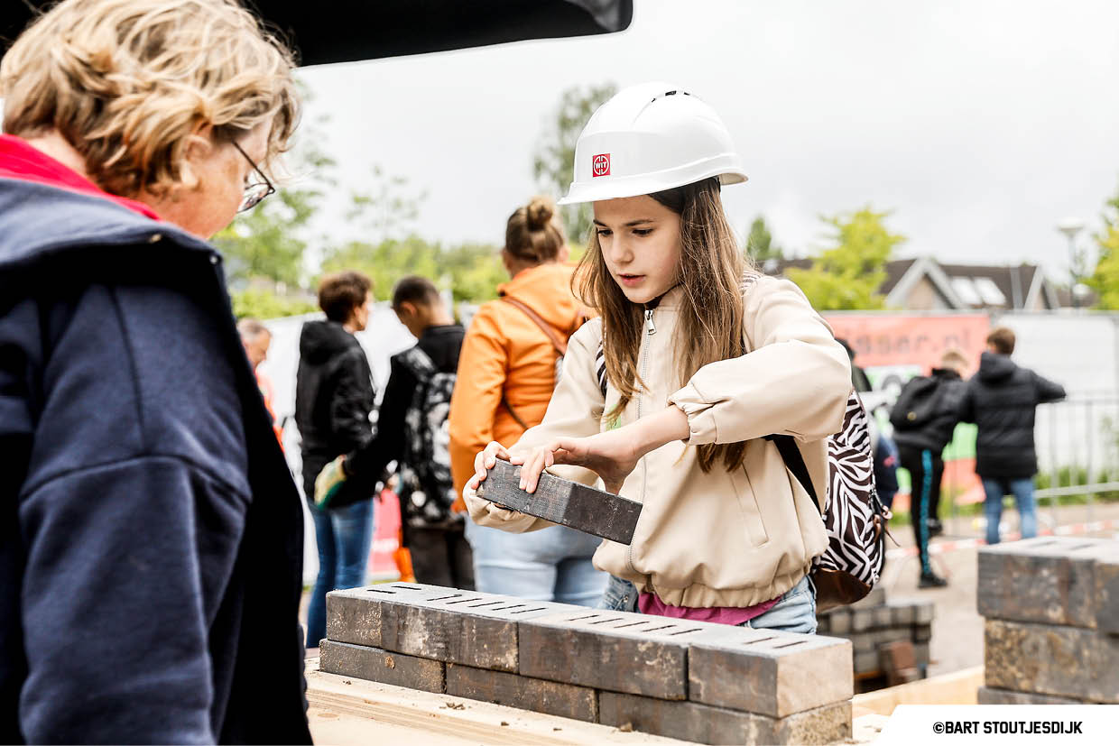 Meisje met helm legt een steen tijdens de Onderwijsdag van de bouw