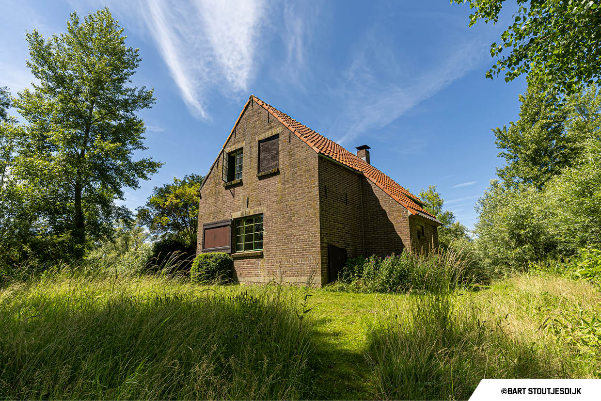 Bakstenen keet met pannendak omgeven door groen