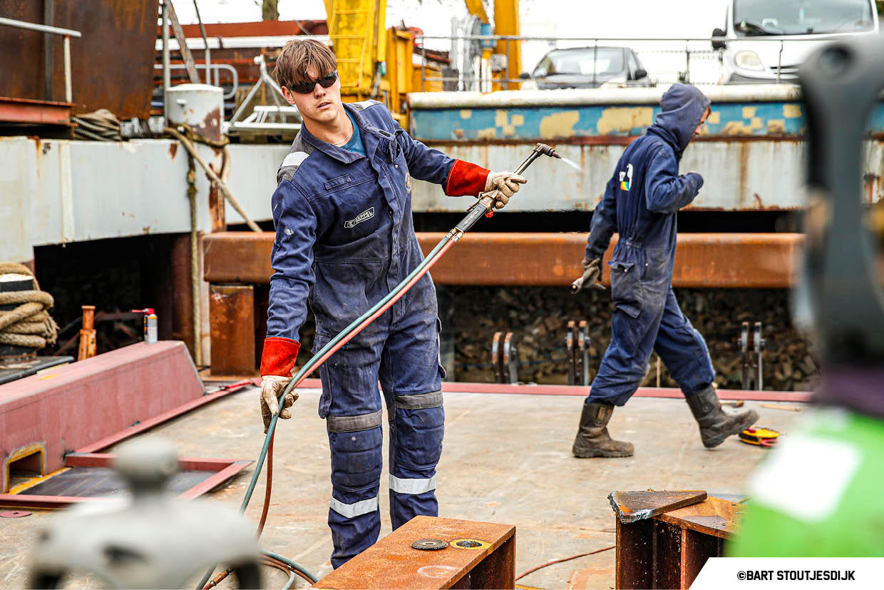 Medewerker in overall en veiligheidsbril houdt een brandende snijbrander vast op het stalen dek van een schip