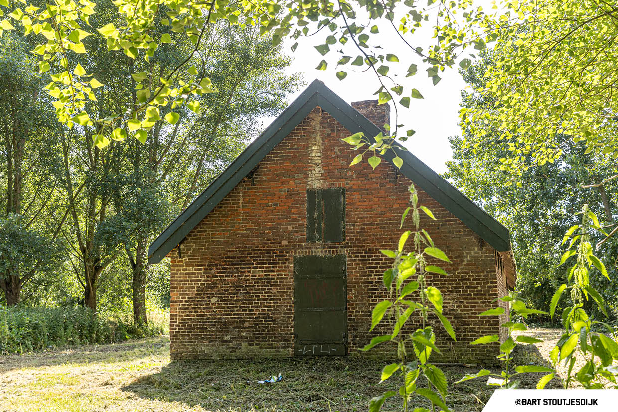 Gevel van een bakstenen keet tussen de bomen