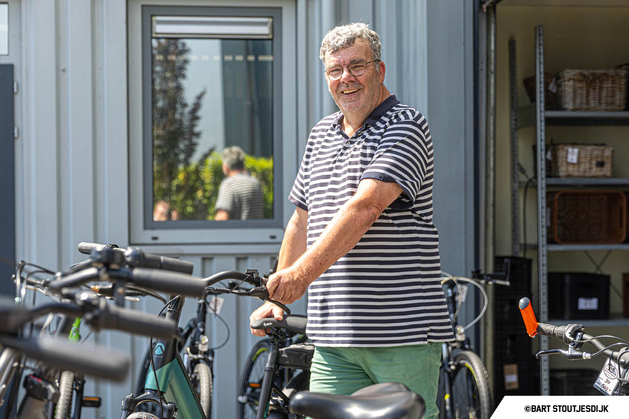 Glimlachende man staat bij een rij fietsen naast een opslagcontainer