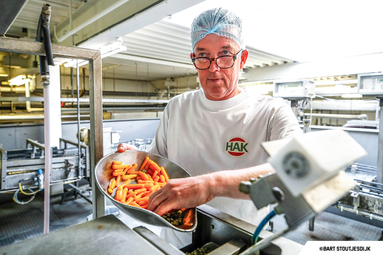 Medewerker houdt een schep met worteltjes en doperwten vast tijdens de kwaliteitscontrole