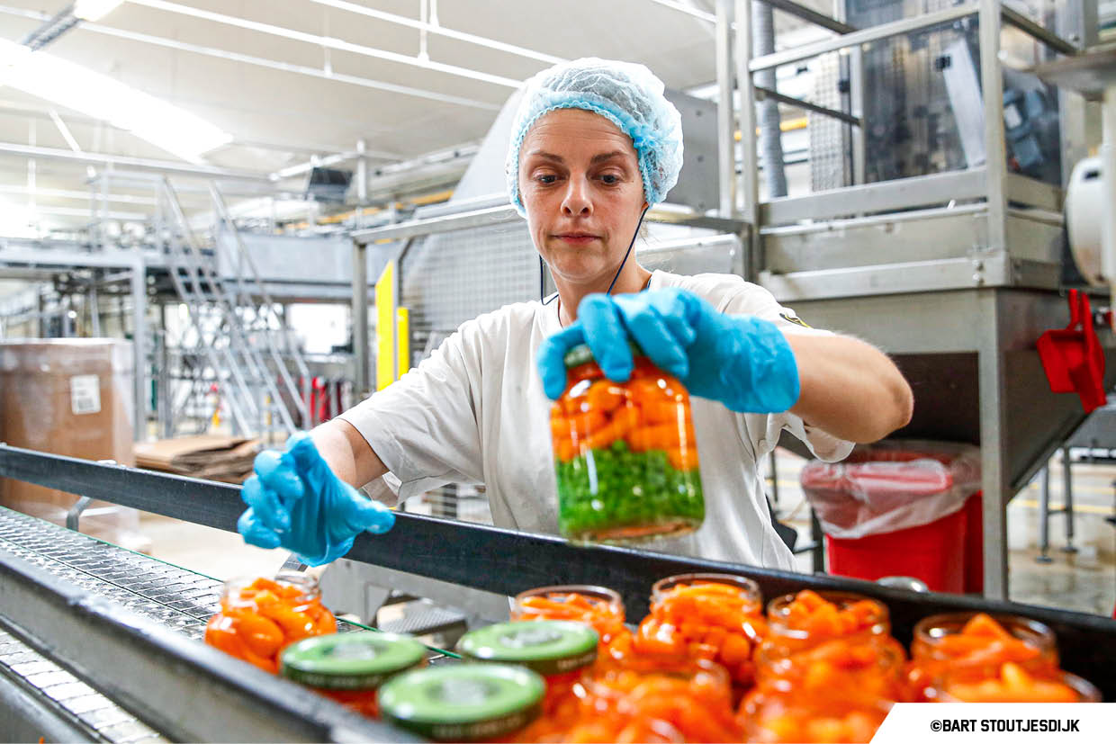 Medewerkster controleert potten peentjes en erwtjes aan de productielijn bij HAK