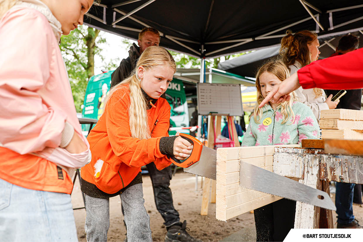 Meisje zaagt aan een houten plank op de Onderwijsdag van de bouw