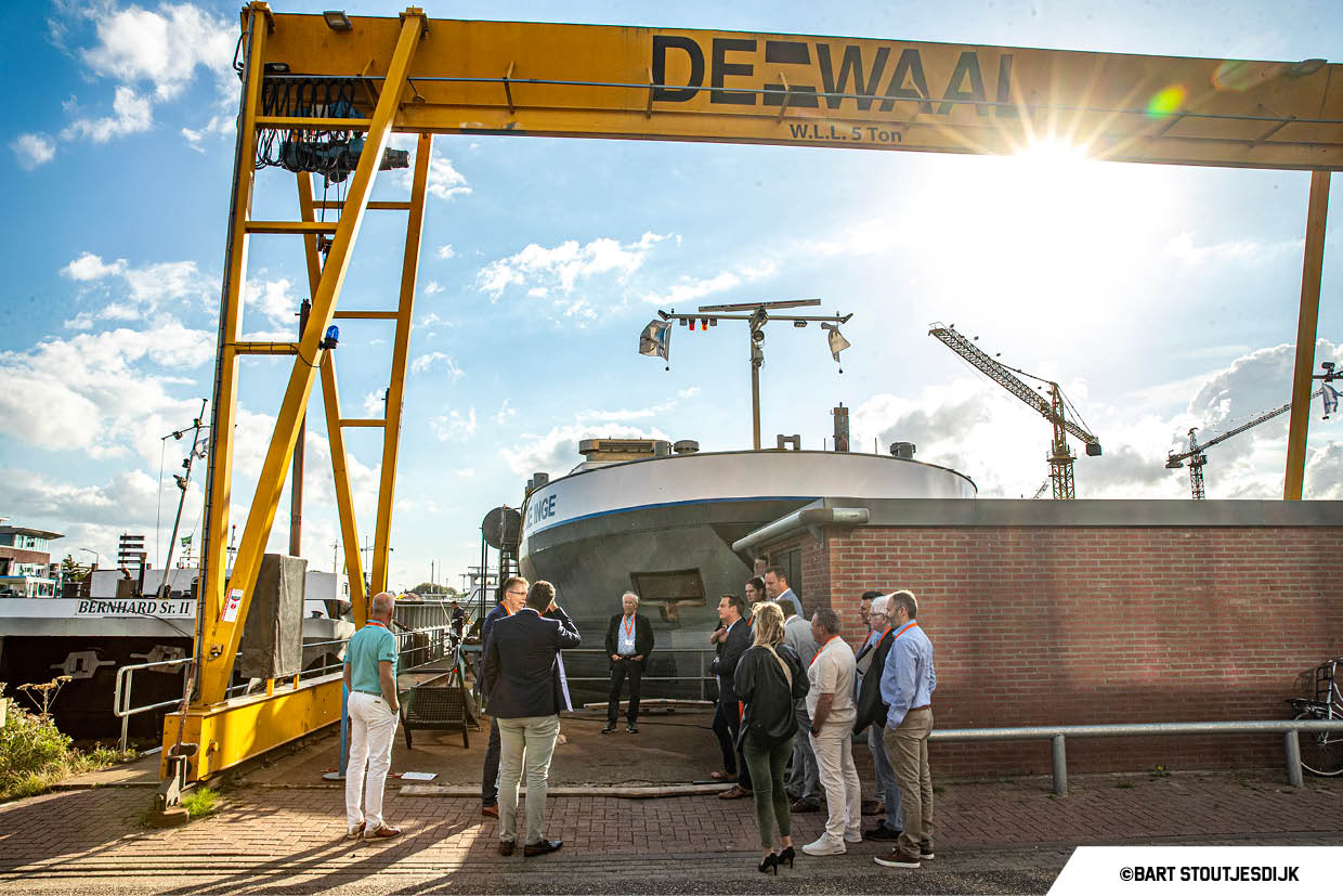 Groep bezoekers bij de boeg van een binnenschip op Scheepswerf De Waal, onder de gele portaalkraan