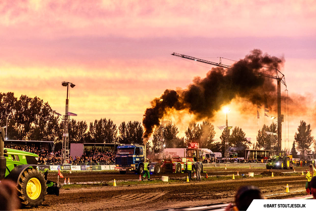 Een blauwe Scania trekt een slee door het zand tijdens een trucktrekwedstrijd bij zonsondergang