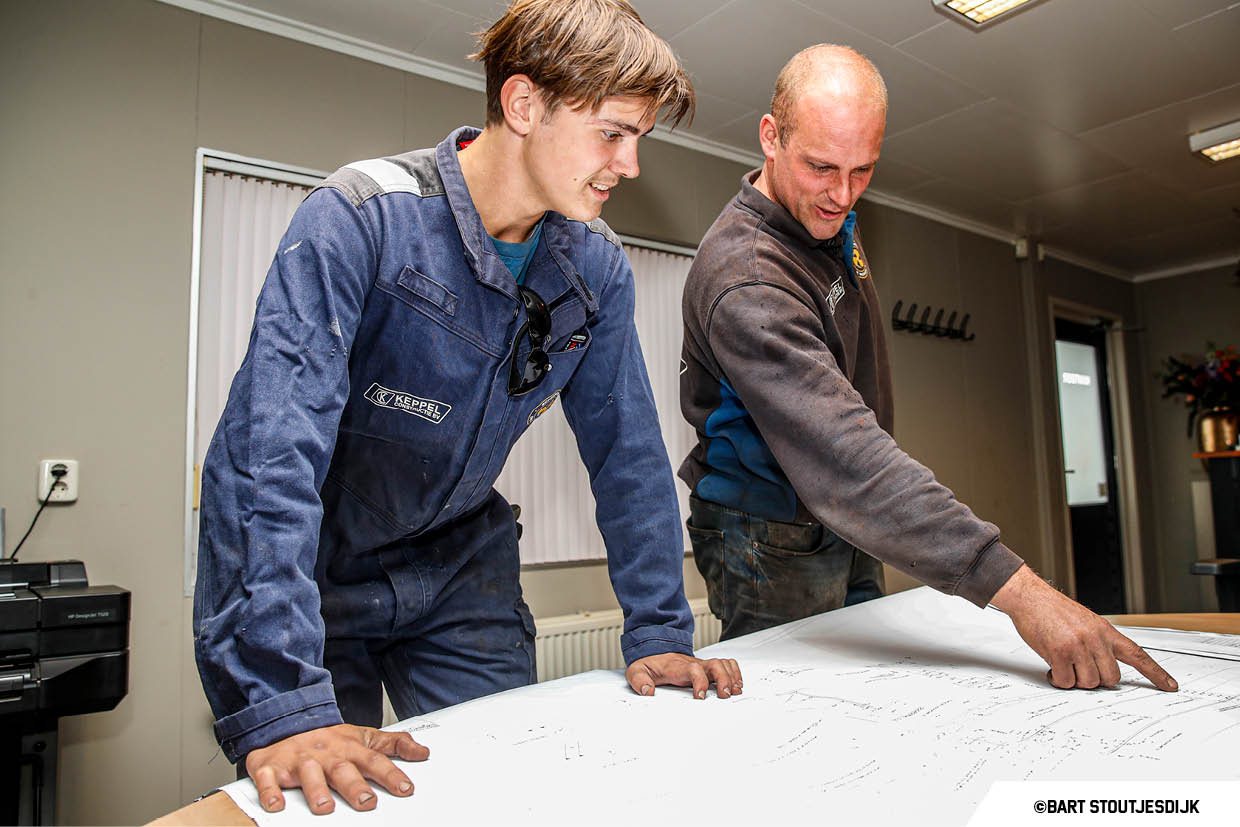 Twee collega's bukken zich samen over een grote technische tekening bij Keppel Constructie